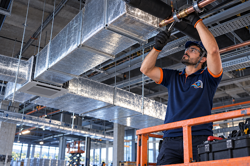 Técnico da Cupecê em uniforme oficial ajustando infraestrutura e tubulações técnicas suspensas no teto industrial